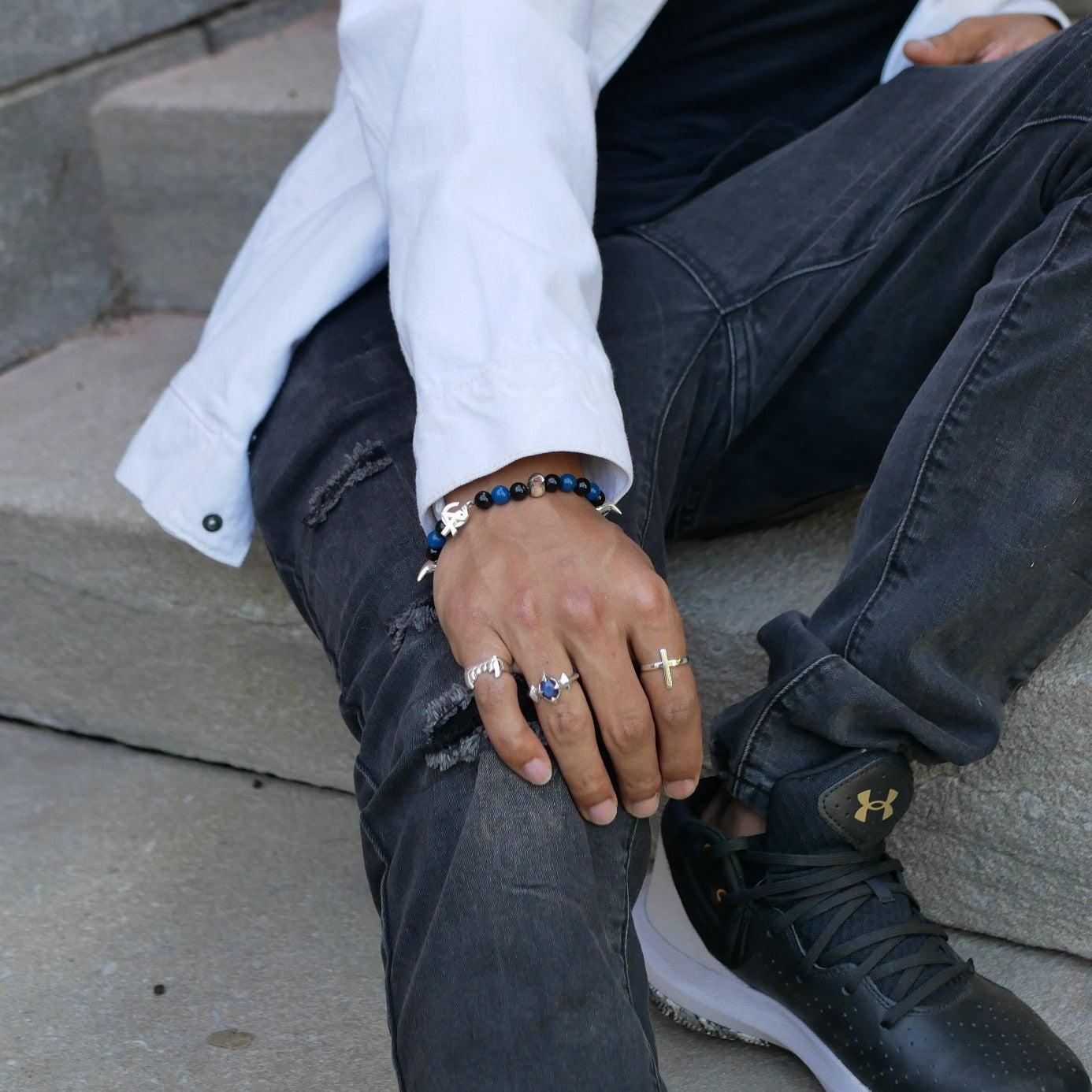 A man sitting in stair with his hand on his knee showing three ring and the Wild crown bracelet on his wrist