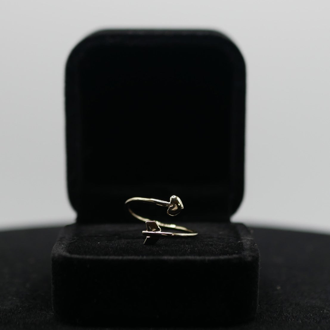 A gold ring that look like an arrow with a heart in a black jewelry box
