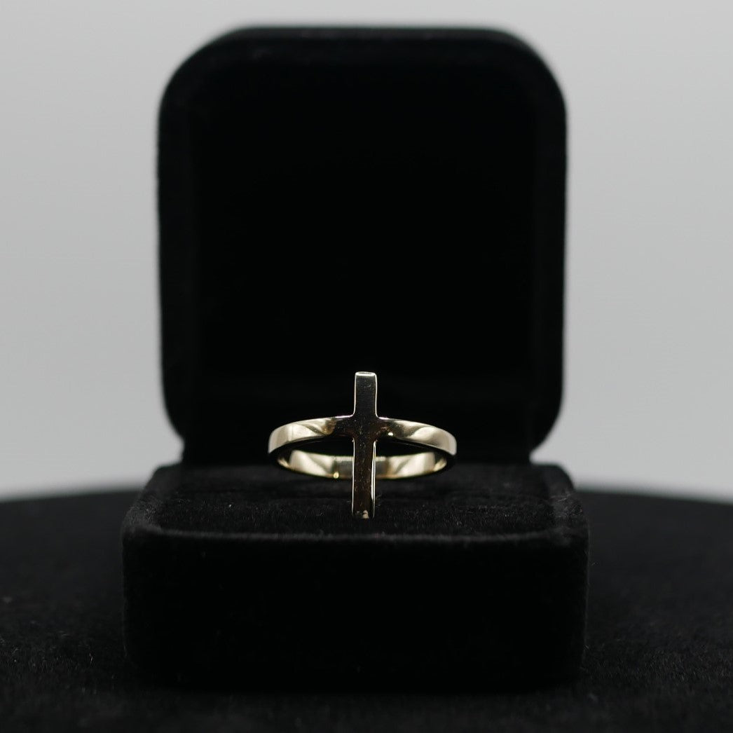 A gold ring shaped in a cross displayed in a jewelry box