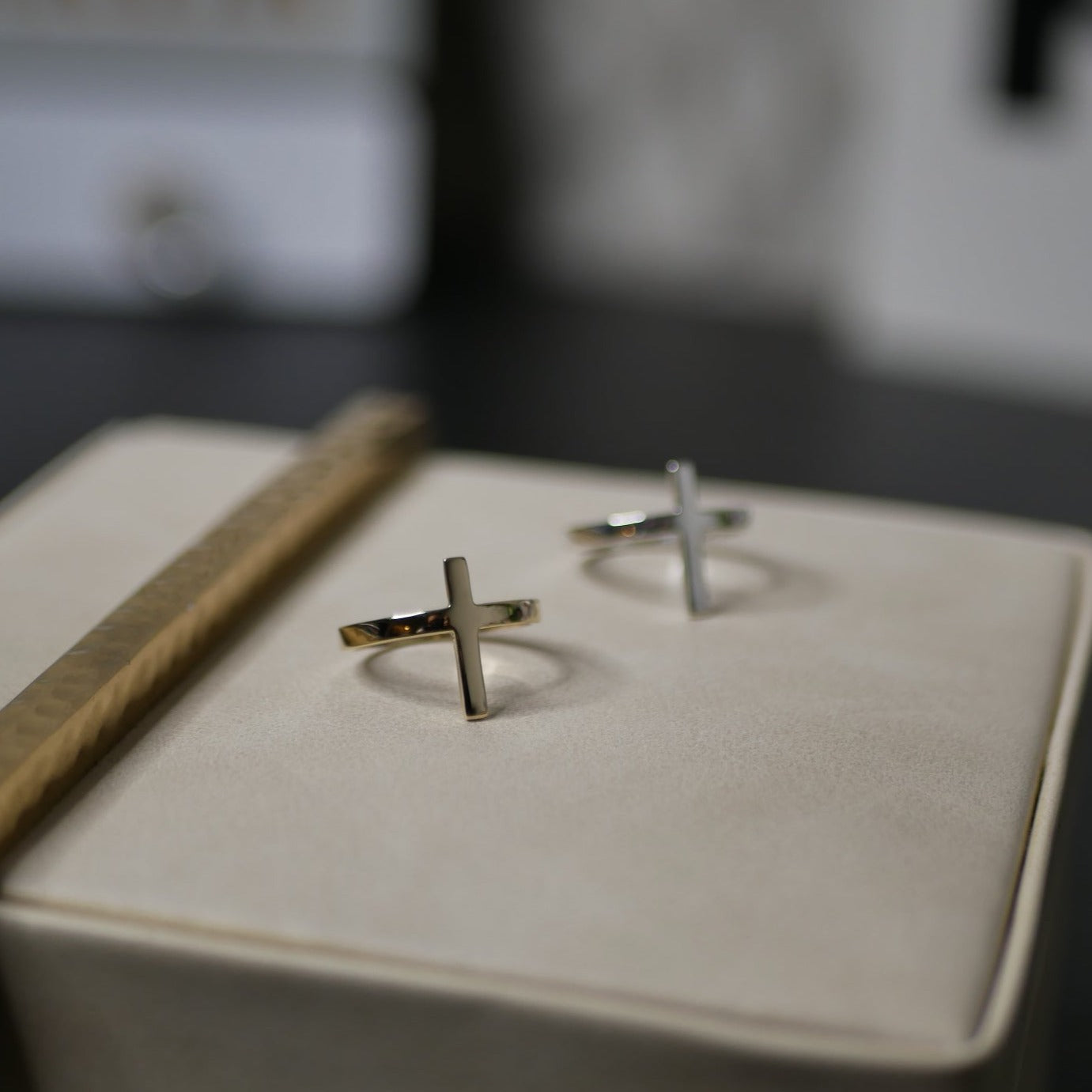 A faith gold ring in the shape of a cross with another silver ring on the top of a jewelry box