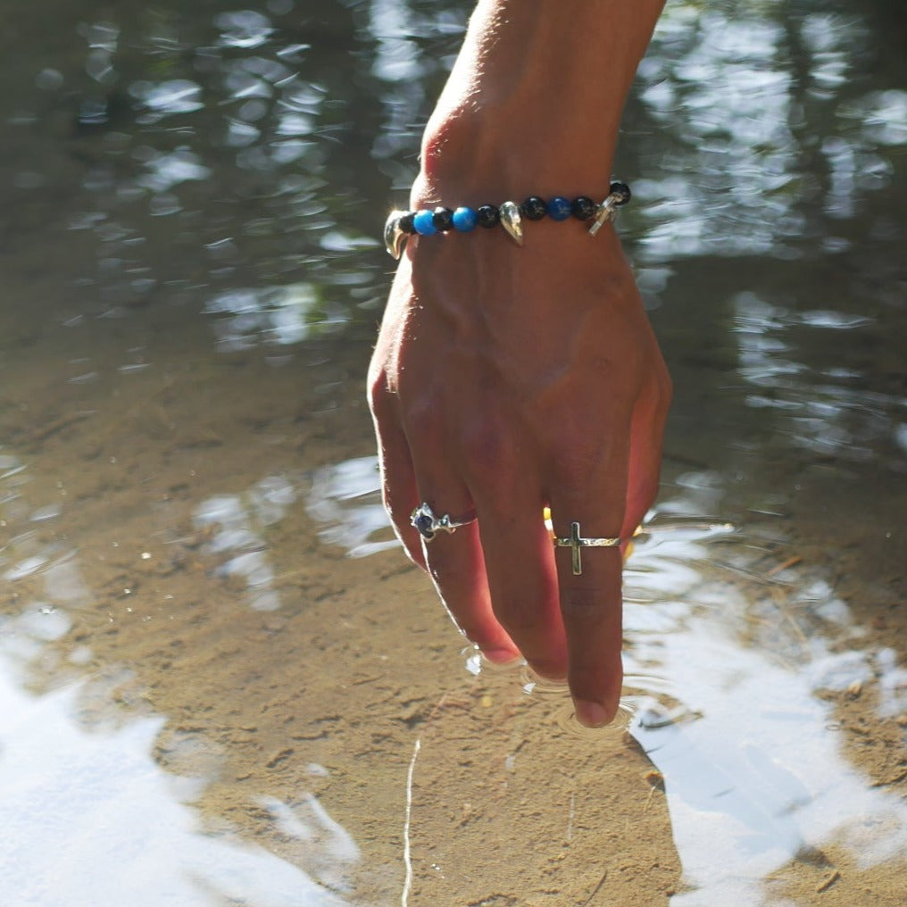 A black man hand touching a river water with his hand showing a cross ring and a silver ring with a blue stone on his finger.