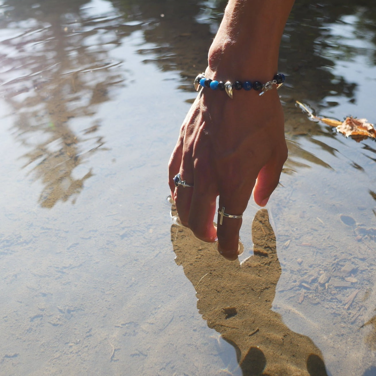 A black man hand with two ring on his finger a the wild crown bracelet on in wrist putting his finger in a river.