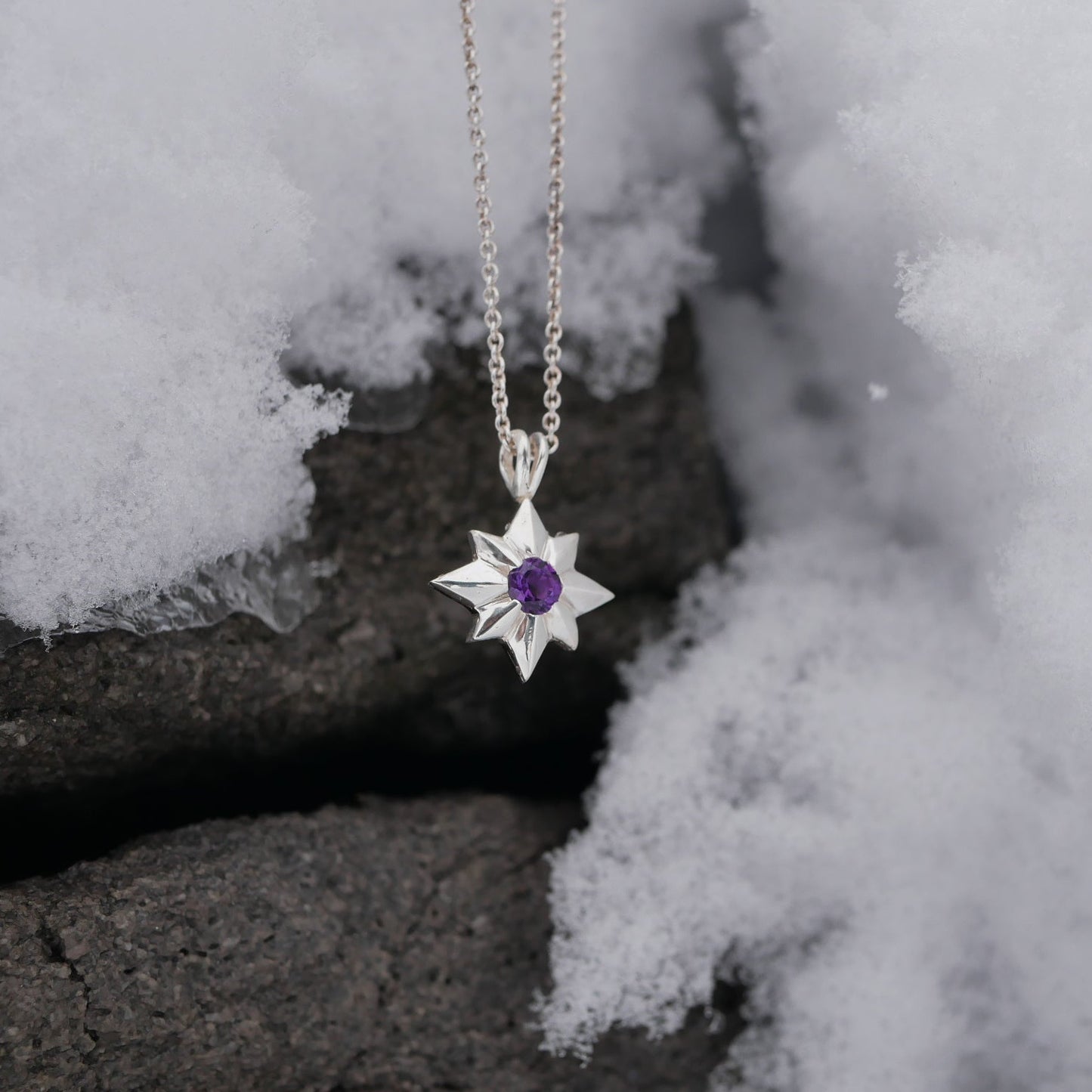 Star-shaped silver pendant with a purple gemstone on a chain, placed on snow.