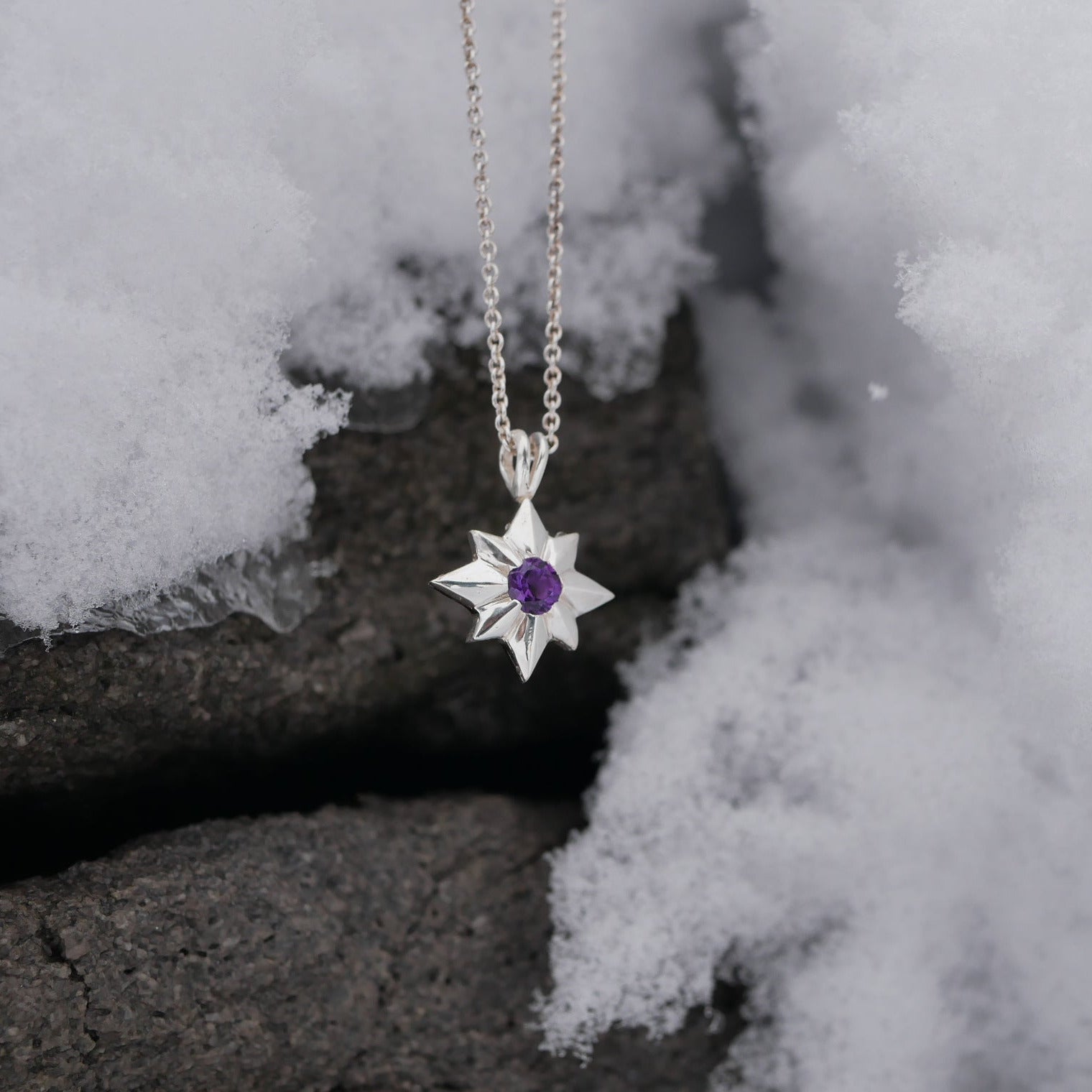 Star-shaped silver pendant with a purple gemstone on a chain, placed on snow.