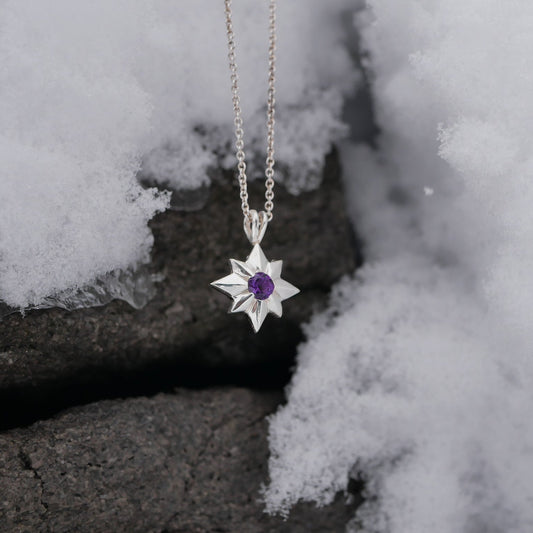 Star-shaped silver pendant with a purple gemstone on a chain, placed on snow.