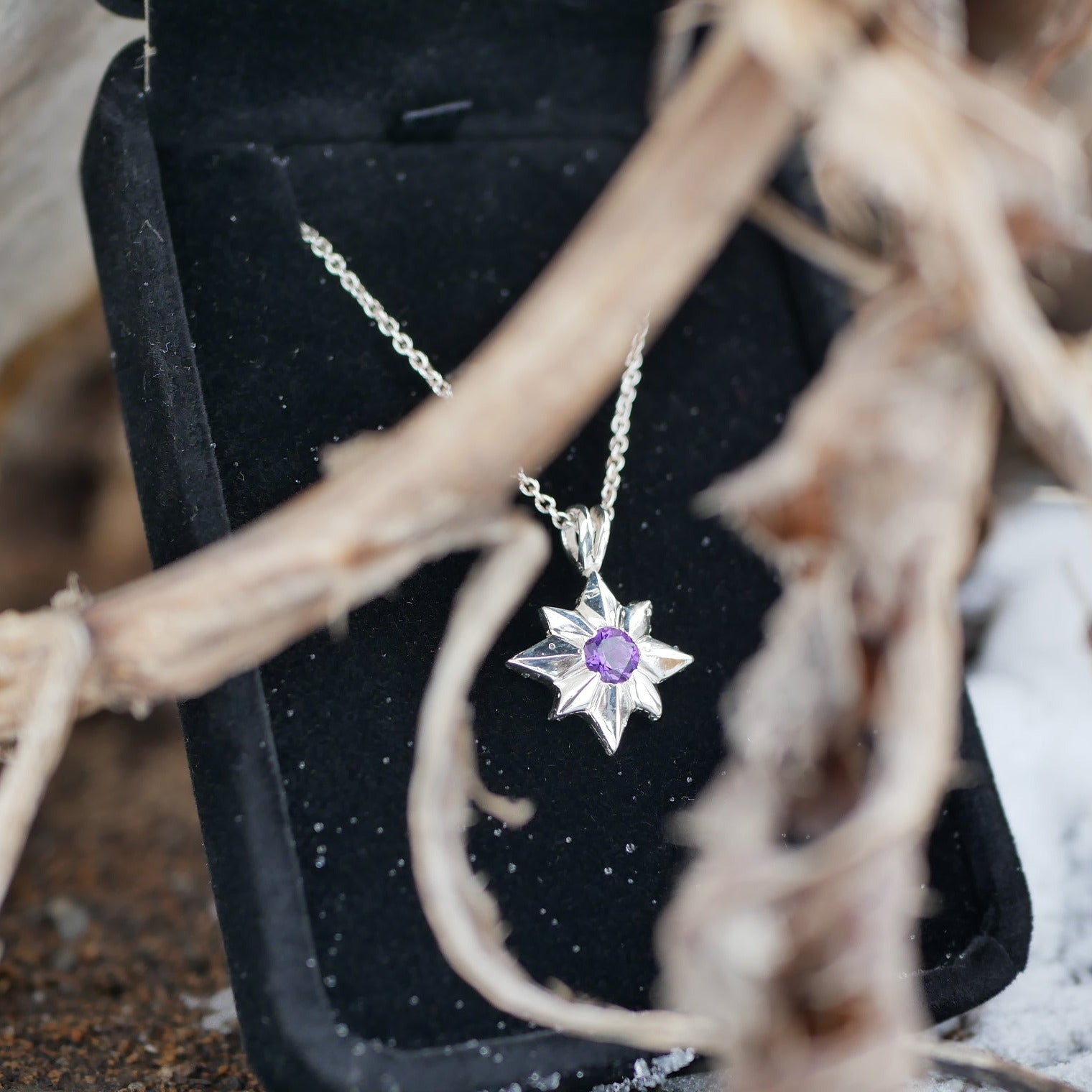 Star-shaped pendant with a purple gemstone in a black box on a natural background