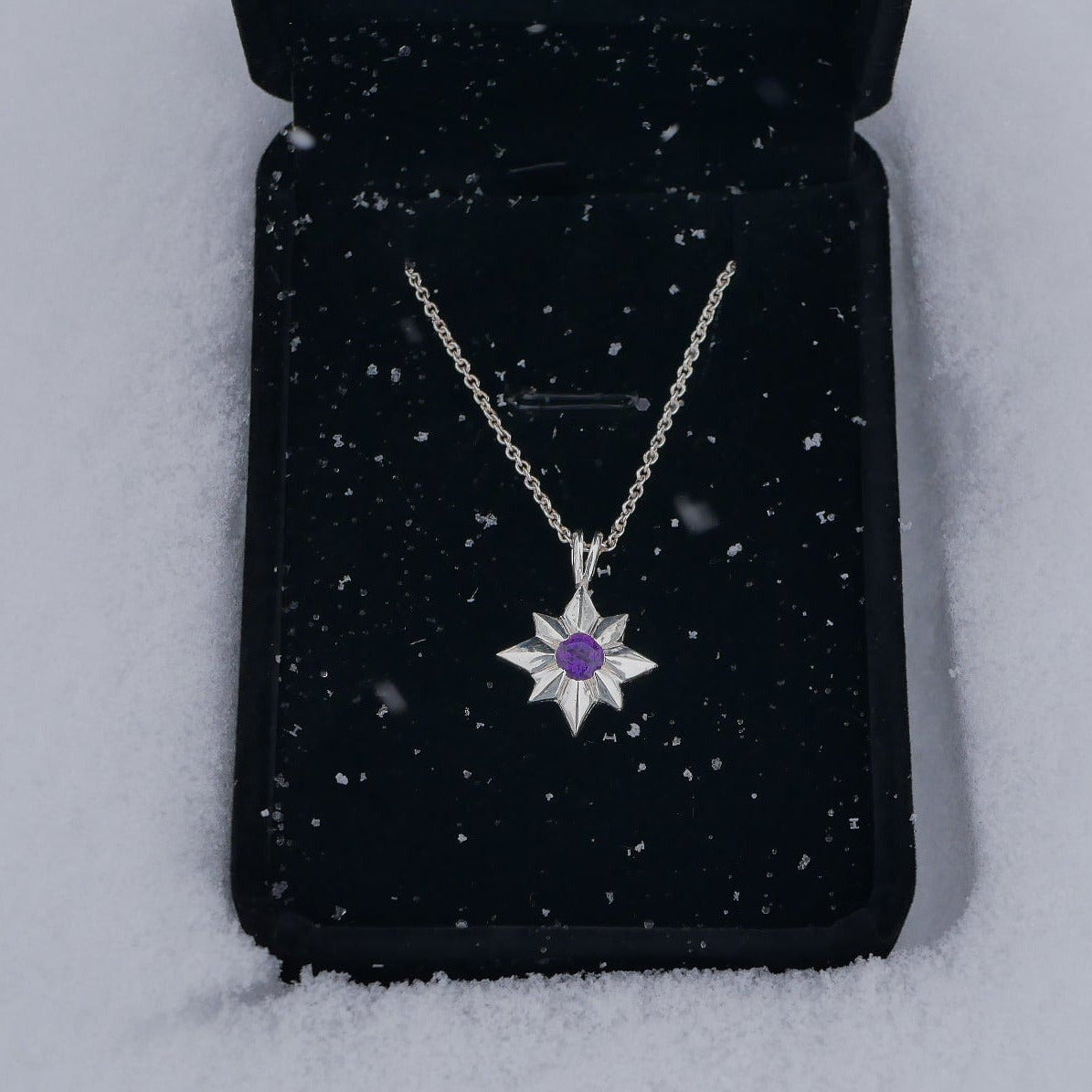 Silver necklace with a purple gemstone on a black jewelry pouch against a snowy background