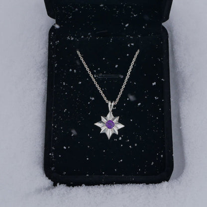 Silver necklace with a purple gemstone on a black jewelry pouch against a snowy background