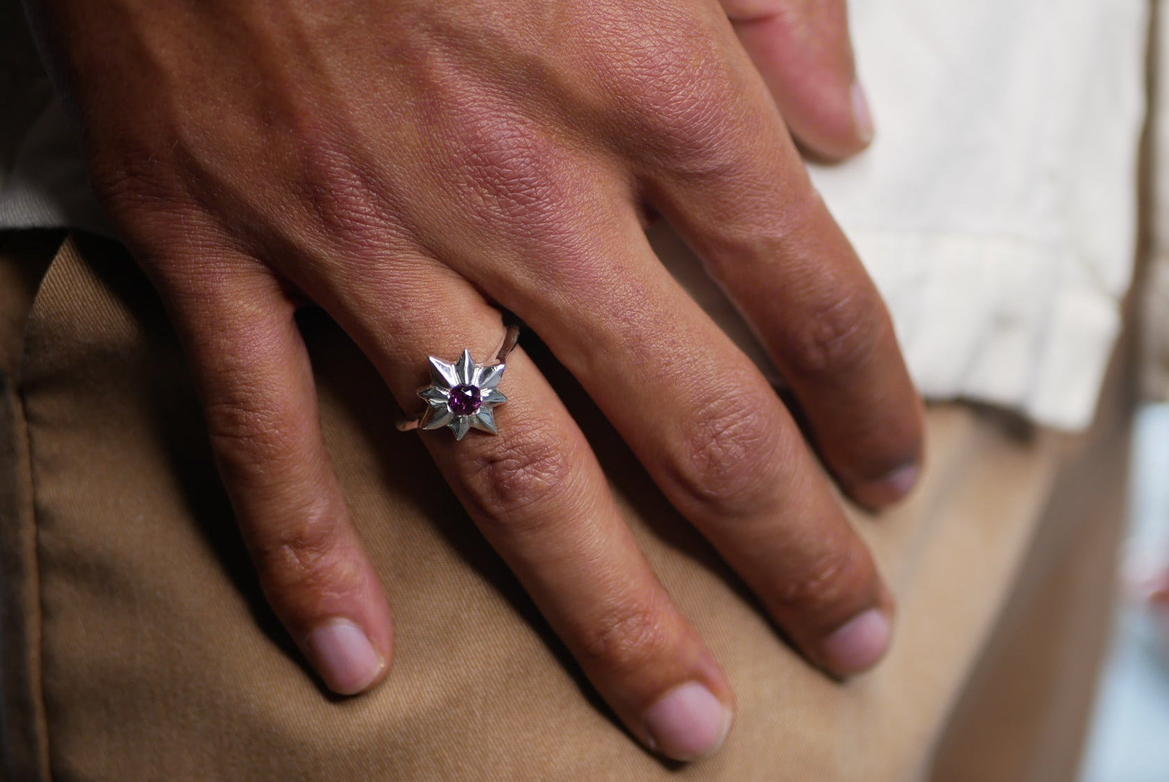 A close-up of a person's hand resting on their lap, wearing a silver-toned ring with a dark red gemstone in a starburst or flower-like setting.